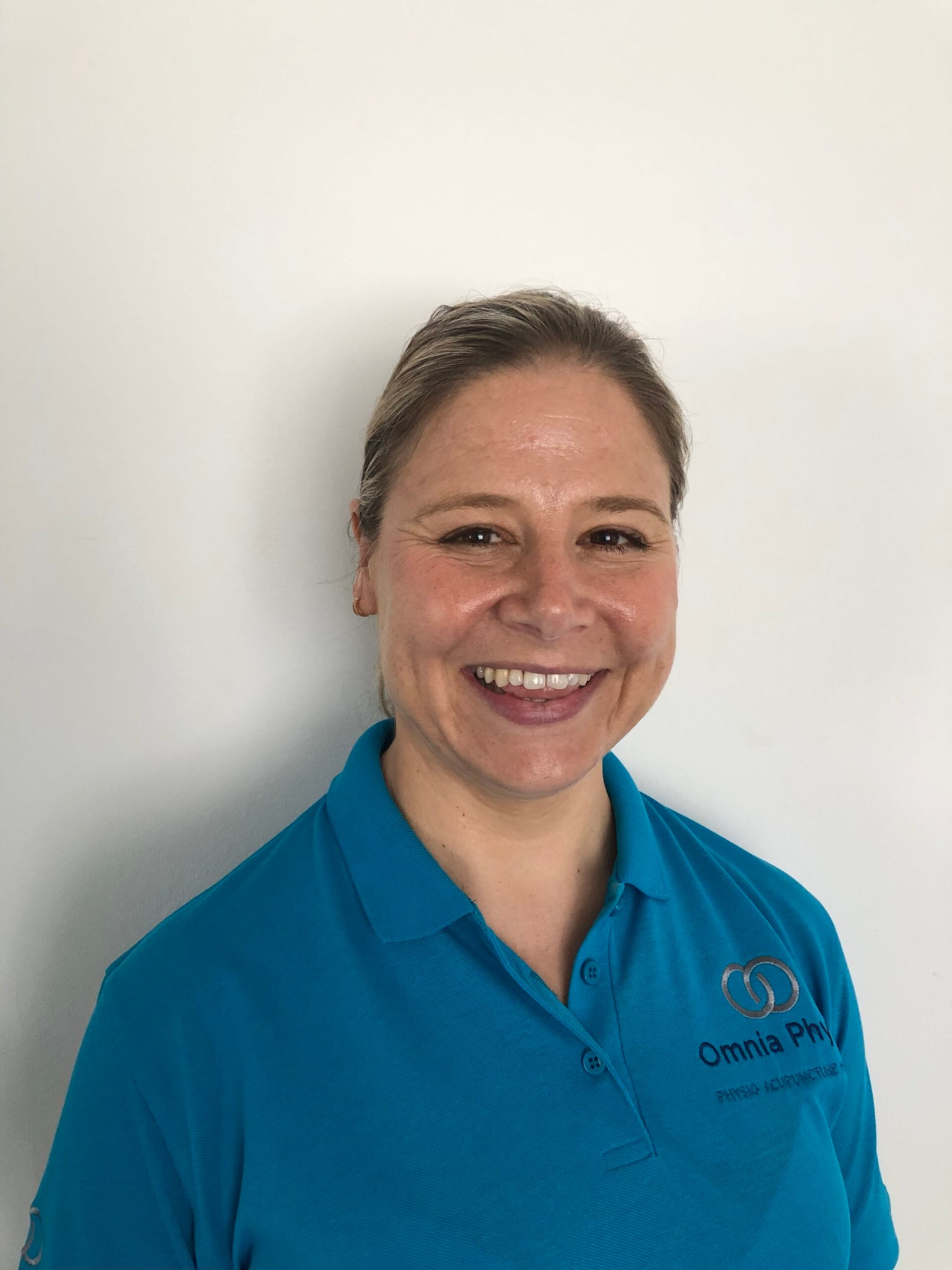 Smiling woman in teal polo against white wall