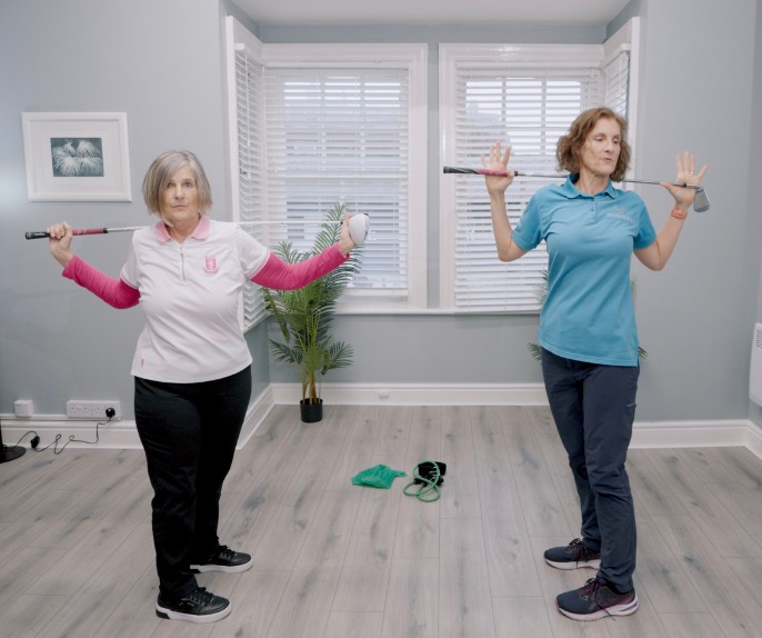 Two women exercising with golf clubs indoors