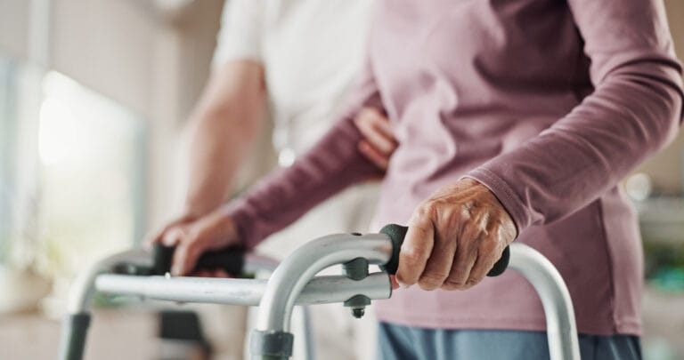 Elderly woman using walking frame with caregiver support