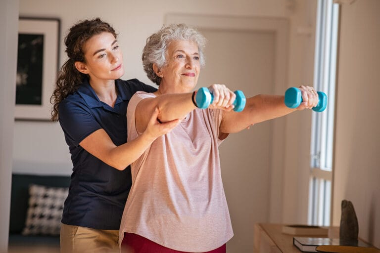 Physiotherapist assisting elderly woman with dumbbell exercises