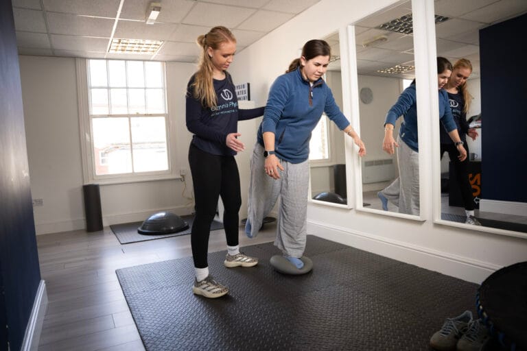 Physiotherapist assisting woman balancing on wobble cushion
