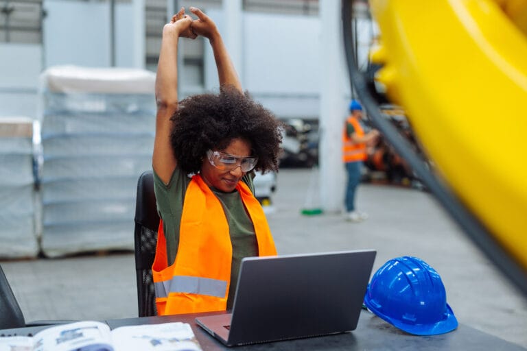 Construction worker stretching at laptop in warehouse