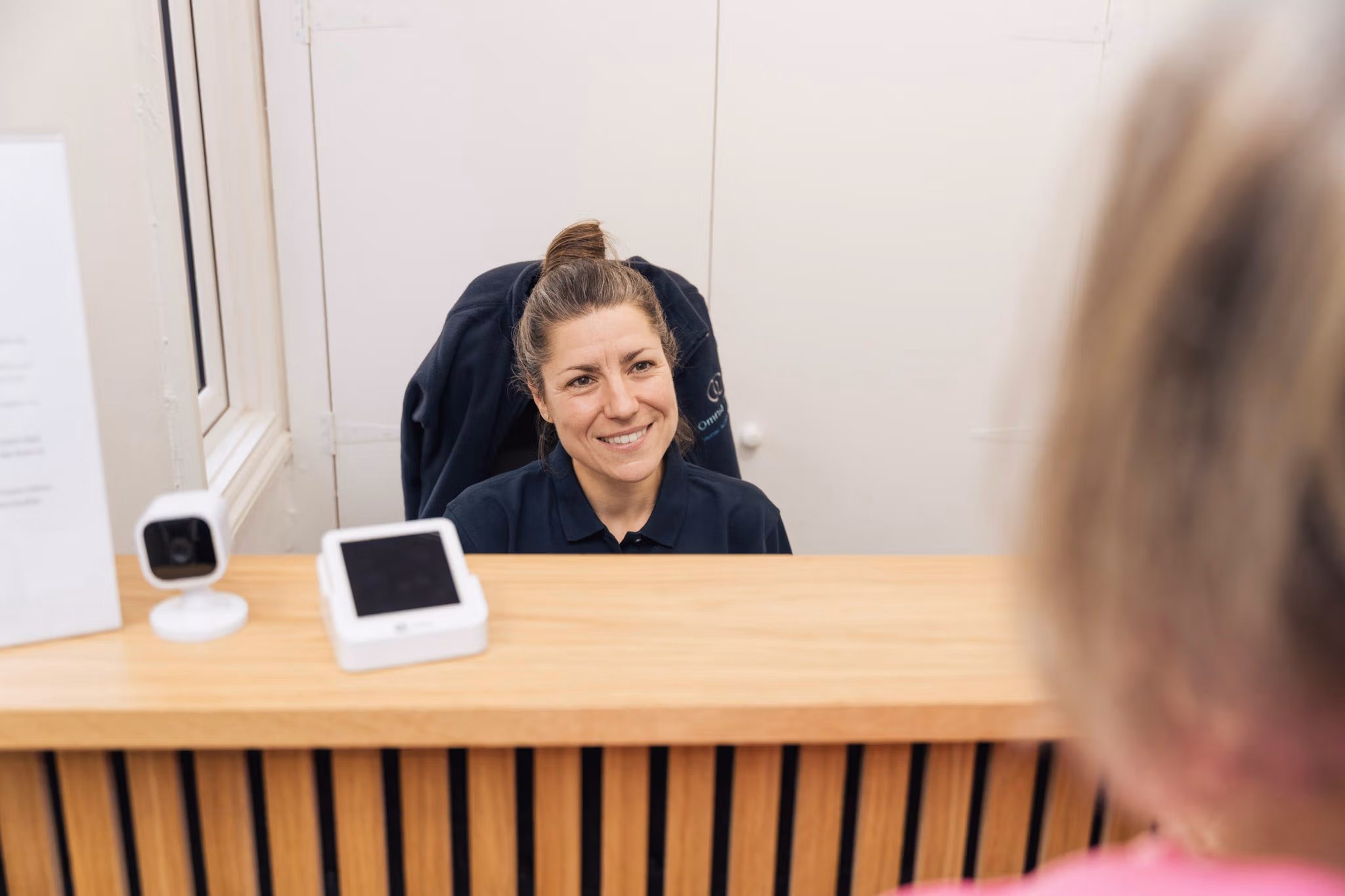 Smiling receptionist assisting visitor at a wooden reception desk