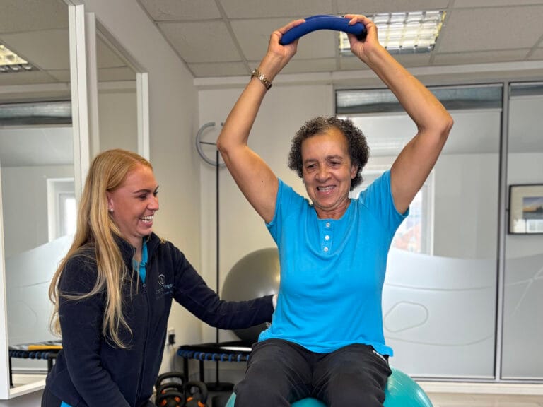Physiotherapist supports woman exercising with resistance ring on stability ball