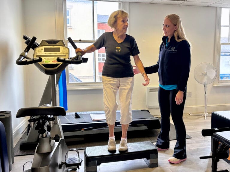 Physiotherapist assisting older woman exercising on vibration platform