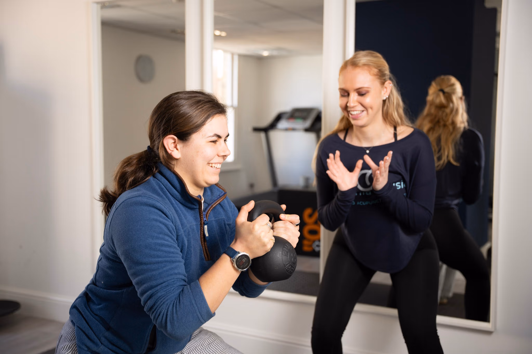 Woman exercises with kettlebell beside encouraging trainer