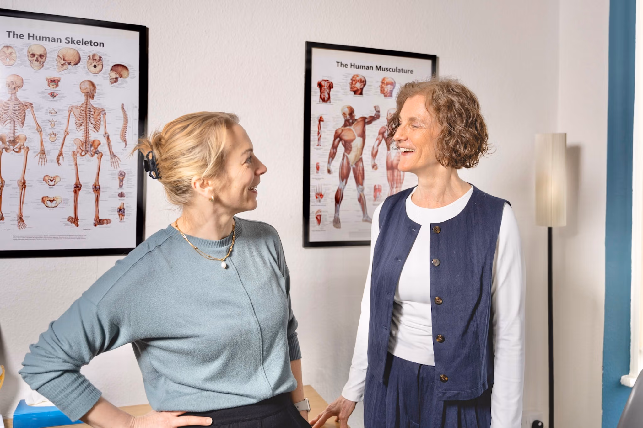 Two women talking beside anatomical skeleton and musculature posters