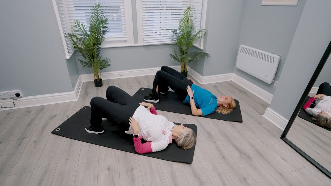 An Omnia physiotherapist and a client doing a bridge exercise on mats